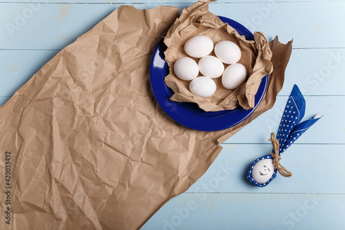 Eggs on paper and blue plate. Easter bunny made from egg and polka dot napkin ears on wooden blue background. Easter concept. Top view  copy space.