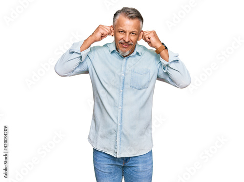 Middle age grey-haired man wearing casual clothes smiling pulling ears with fingers, funny gesture. audition problem