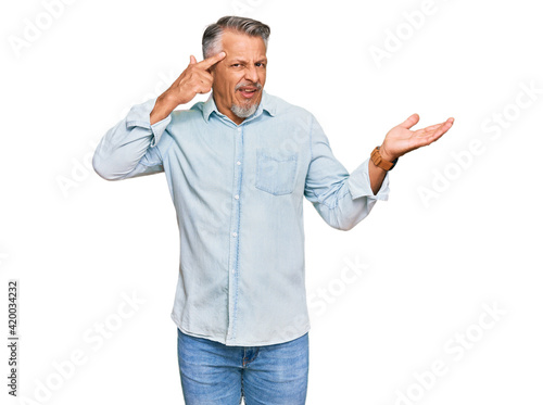 Middle age grey-haired man wearing casual clothes confused and annoyed with open palm showing copy space and pointing finger to forehead. think about it.