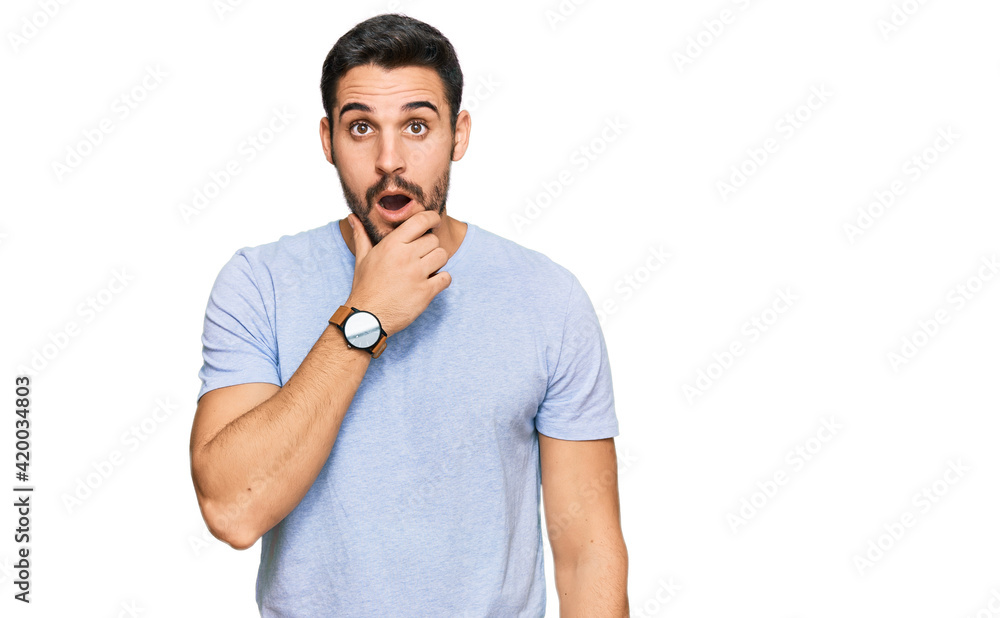 Young hispanic man wearing casual clothes looking fascinated with disbelief, surprise and amazed expression with hands on chin Young hispanic man wearing casual clothes looking fascinated with disbelief, surprise and amazed expression with hands on chin