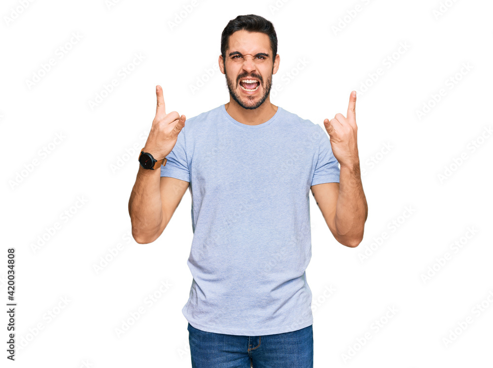 Young hispanic man wearing casual clothes shouting with crazy expression doing rock symbol with hands up. music star. heavy music concept. Young hispanic man wearing casual clothes shouting with crazy expression doing rock symbol with hands up. music star. heavy music concept.