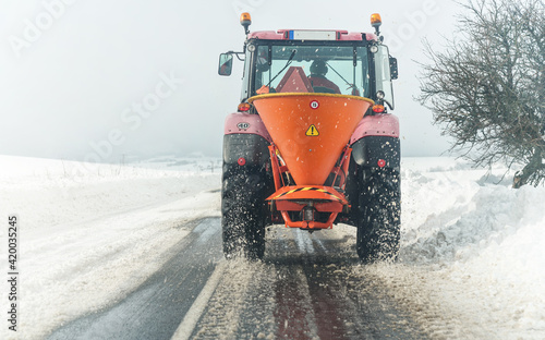 Small gritter maintenance tractor spreading de icing salt on asphalt road, view from car driving behind