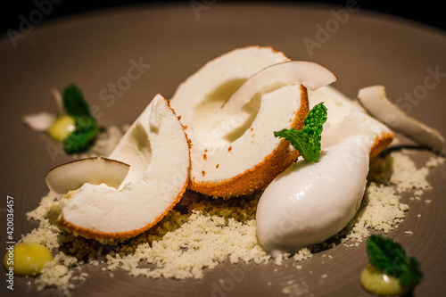 coconut ice cream served with shaved coconut, dessicated coconut and mint on a plate