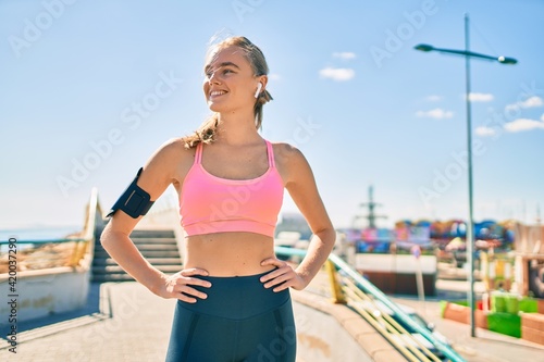 Young blonde sportswoman using earphones doing exercise at the city