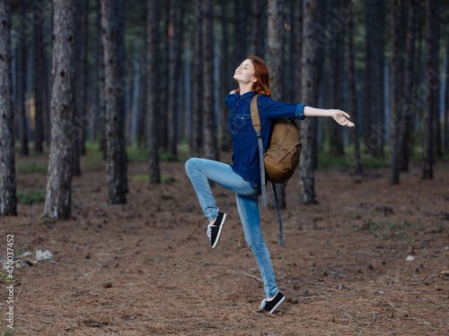 Happy woman having fun in the pine forest with a backpack on her back