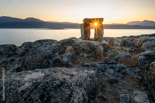 Sunset through Inuksuk in rough arctic landscape. Sunstar on the horizon in the fjord of Qikiqtarjuaq, Broughton Island, Nunavut.