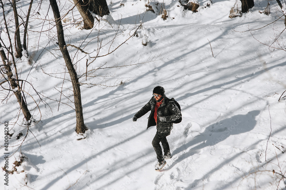 An adult man, a wanderer, a tourist in black clothes with a backpack on his back walks through the snowy forest, enjoying the beautiful nature. Photography, concept.