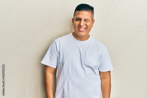 Young latin man wearing casual white t shirt winking looking at the camera with sexy expression, cheerful and happy face.