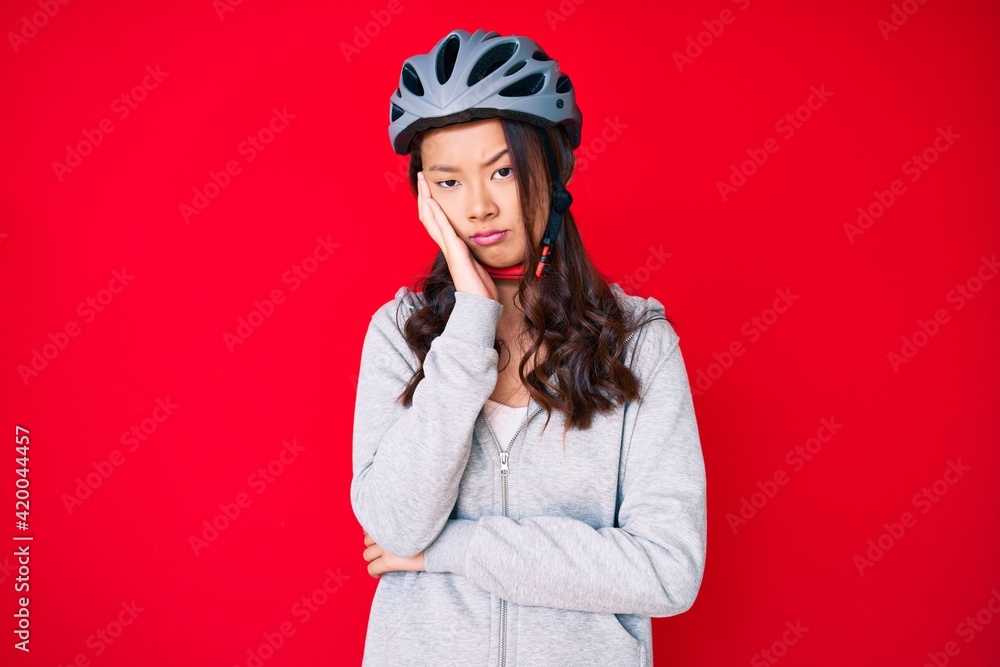 Young beautiful chinese girl wearing bike helmet thinking looking tired and bored with depression problems with crossed arms.