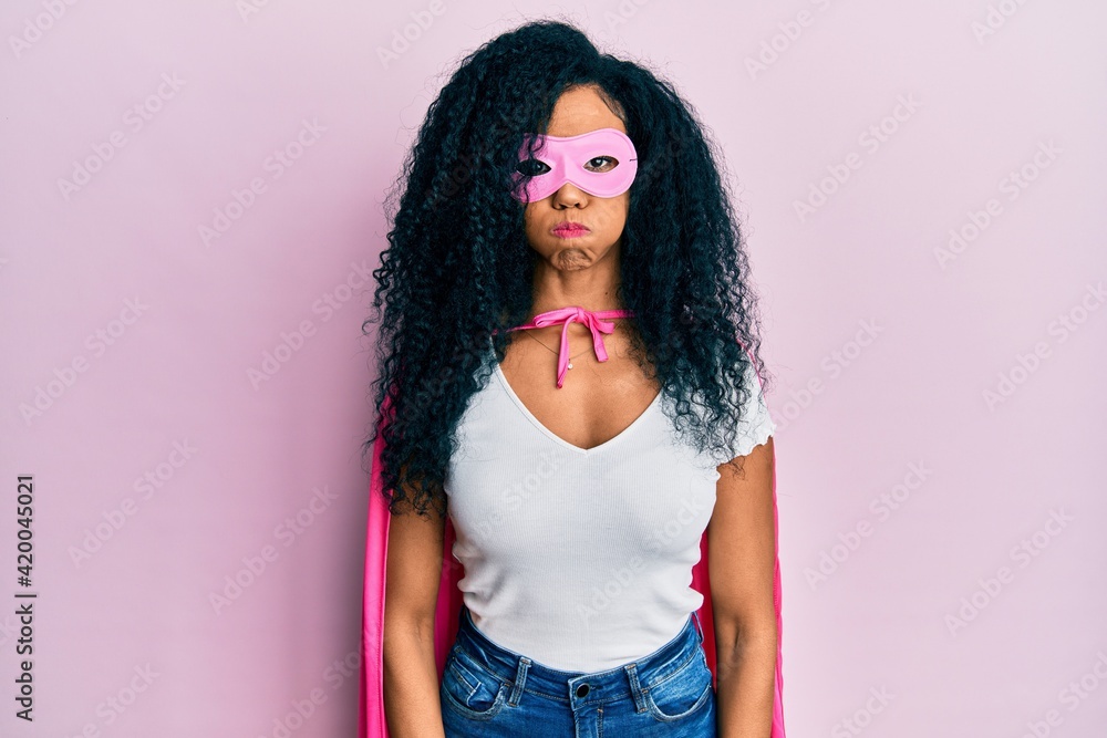 Middle age african american woman wearing super hero costume puffing cheeks with funny face. mouth inflated with air, crazy expression. Middle age african american woman wearing super hero costume puffing cheeks with funny face. mouth inflated with air, crazy expression.