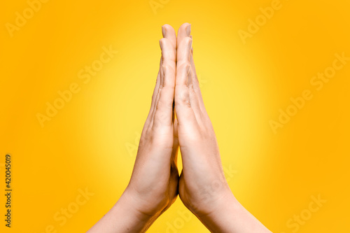 women's hands folded in prayer on a yellow background