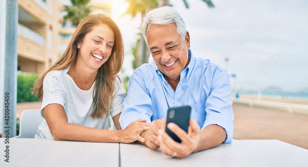Middle age couple in love sitting at the terrace of coffee shop using smartphone happy and cheerful together Middle age couple in love sitting at the terrace of coffee shop using smartphone happy and cheerful together