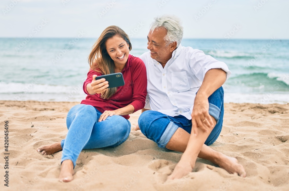 Middle age hispanic couple making selfie by the smartphone at the beach. Middle age hispanic couple making selfie by the smartphone at the beach.