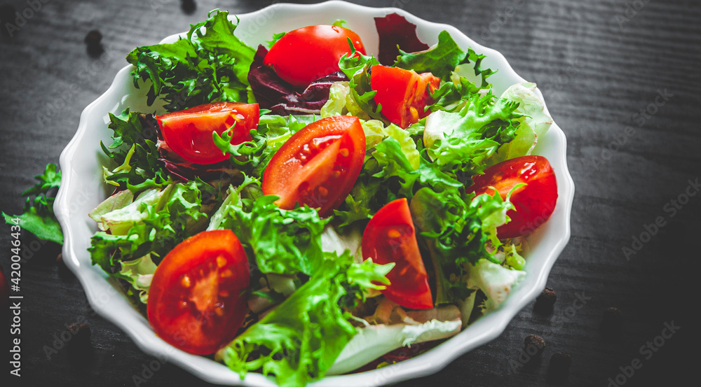 various fresh mix salad leaves with tomato in bowl on dark wooden background various fresh mix salad leaves with tomato in bowl on dark wooden background