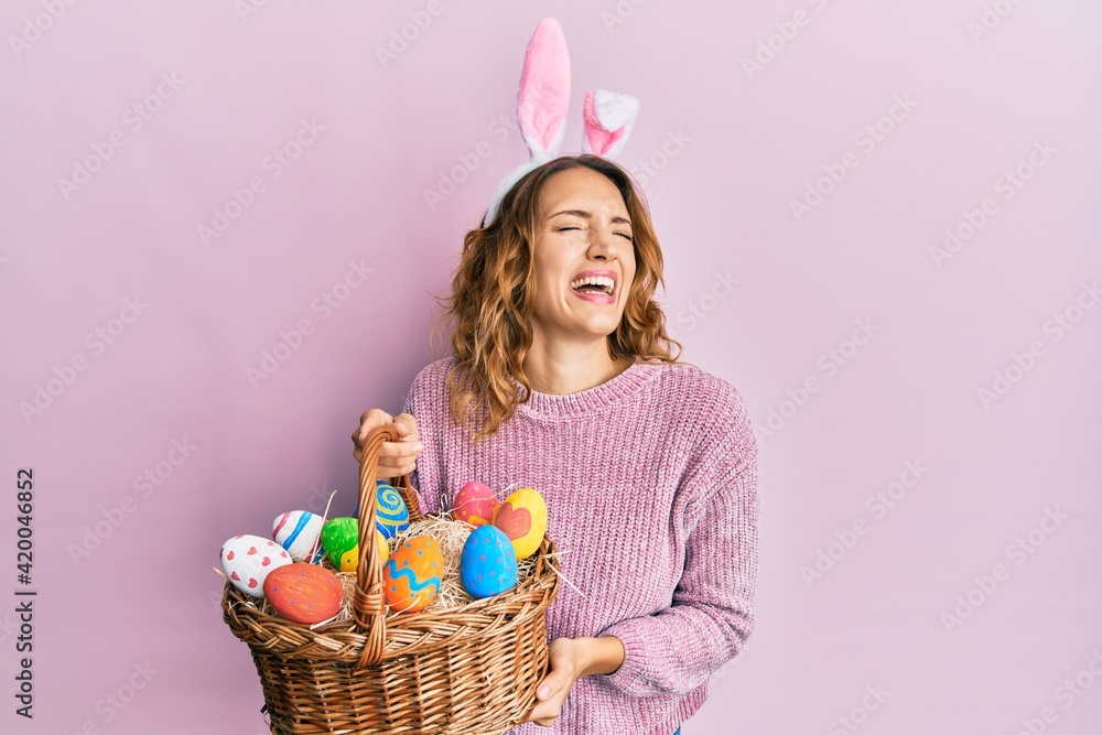 Young caucasian woman wearing cute easter bunny ears holding colored egg smiling and laughing hard out loud because funny crazy joke. Young caucasian woman wearing cute easter bunny ears holding colored egg smiling and laughing hard out loud because funny crazy joke.