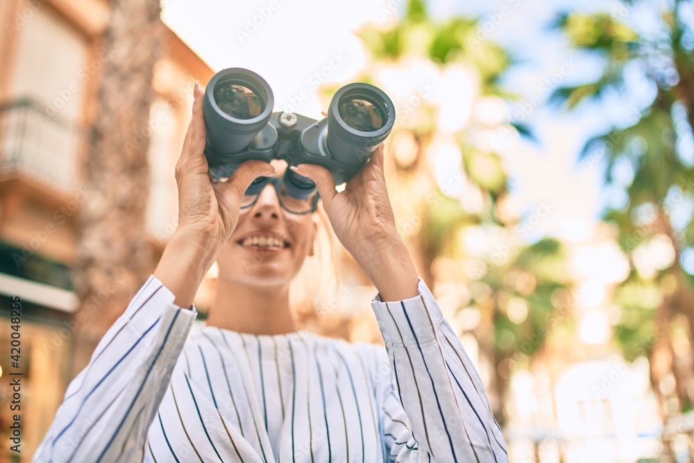 Young blonde businesswoman smiling happy using binoculars at the city. Young blonde businesswoman smiling happy using binoculars at the city.