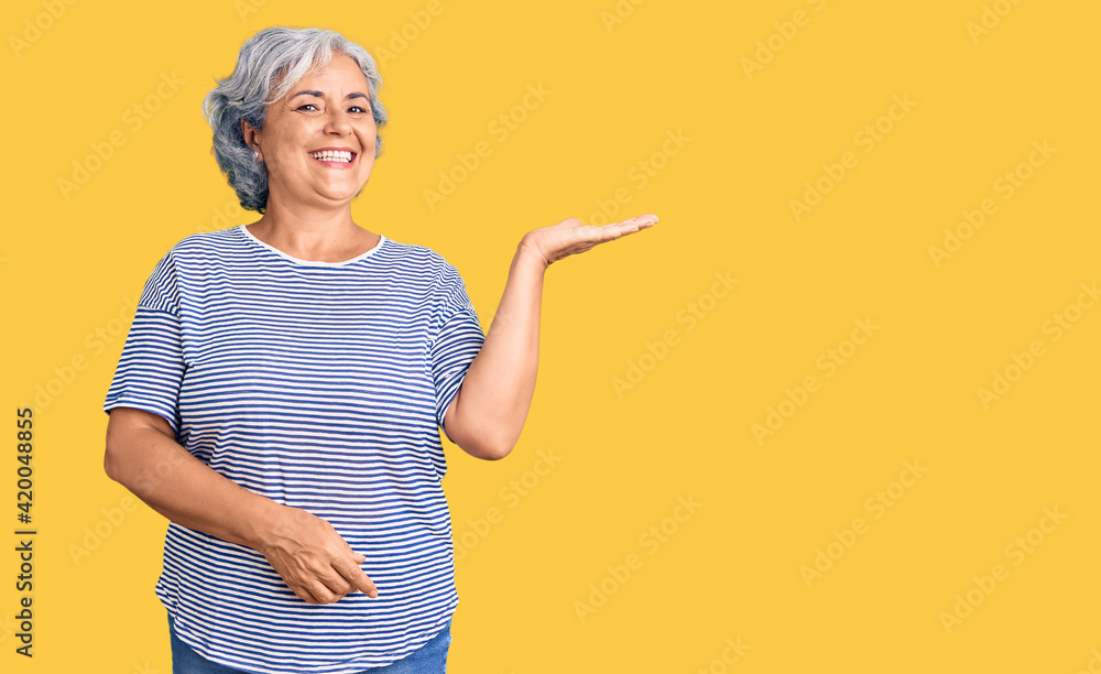 Senior woman with gray hair wearing casual striped clothes smiling cheerful presenting and pointing with palm of hand looking at the camera. Senior woman with gray hair wearing casual striped clothes smiling cheerful presenting and pointing with palm of hand looking at the camera.