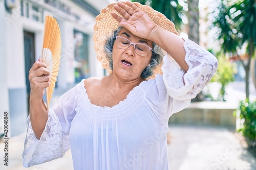 Vászonkép Middle age woman with grey hair using handfan on a very hot day of a heat wave