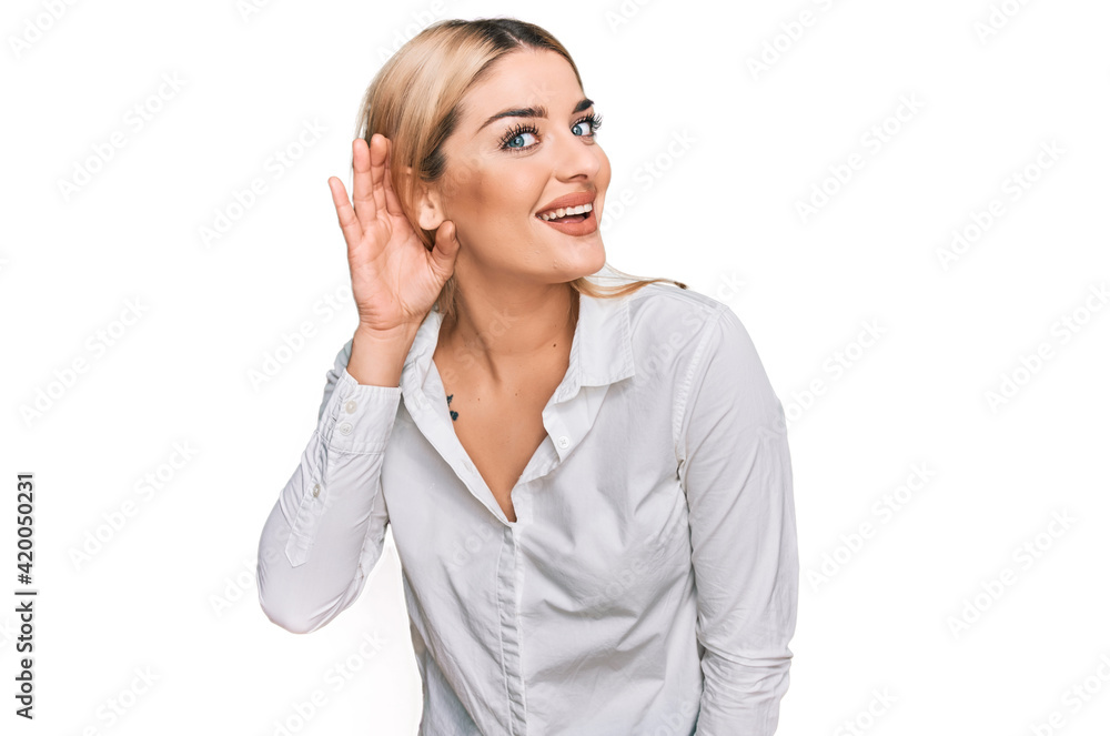 Young caucasian woman wearing casual clothes smiling with hand over ear listening an hearing to rumor or gossip. deafness concept. Young caucasian woman wearing casual clothes smiling with hand over ear listening an hearing to rumor or gossip. deafness concept.