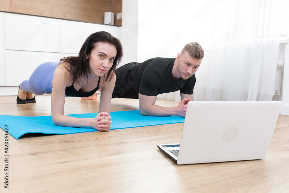 Young couple man and woman doing fitness at home online using laptop, doing online with trainer on floor at home sports Young couple man and woman doing fitness at home online using laptop, doing online with trainer on floor at home sports