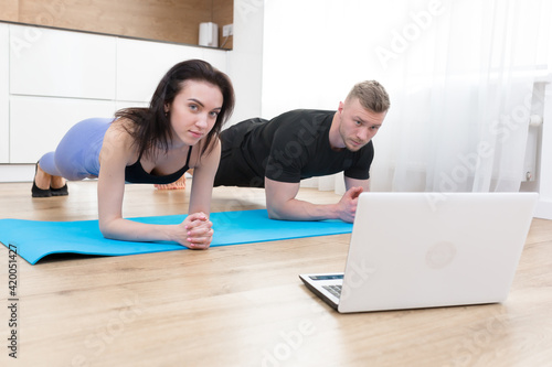 Young couple man and woman doing fitness at home online using laptop, doing online with trainer on floor at home sports