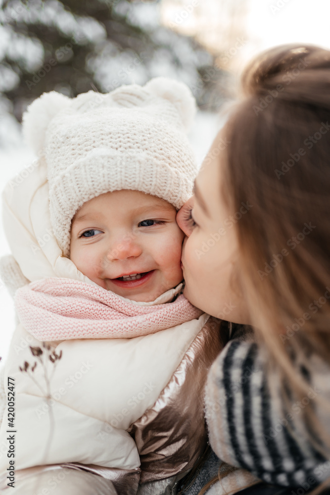 Young mom holding and kissing small beautiful baby girl in winter hat Young mom holding and kissing small beautiful baby girl in winter hat