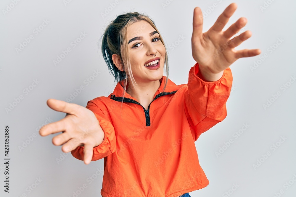 Young modern girl wearing sports sweatshirt looking at the camera smiling with open arms for hug. cheerful expression embracing happiness. Young modern girl wearing sports sweatshirt looking at the camera smiling with open arms for hug. cheerful expression embracing happiness.