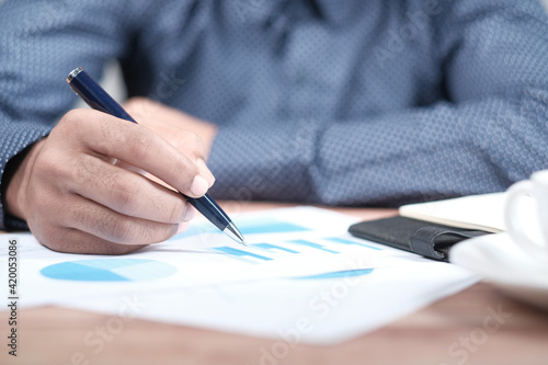 man hand with pen analyzing financial graph on table 