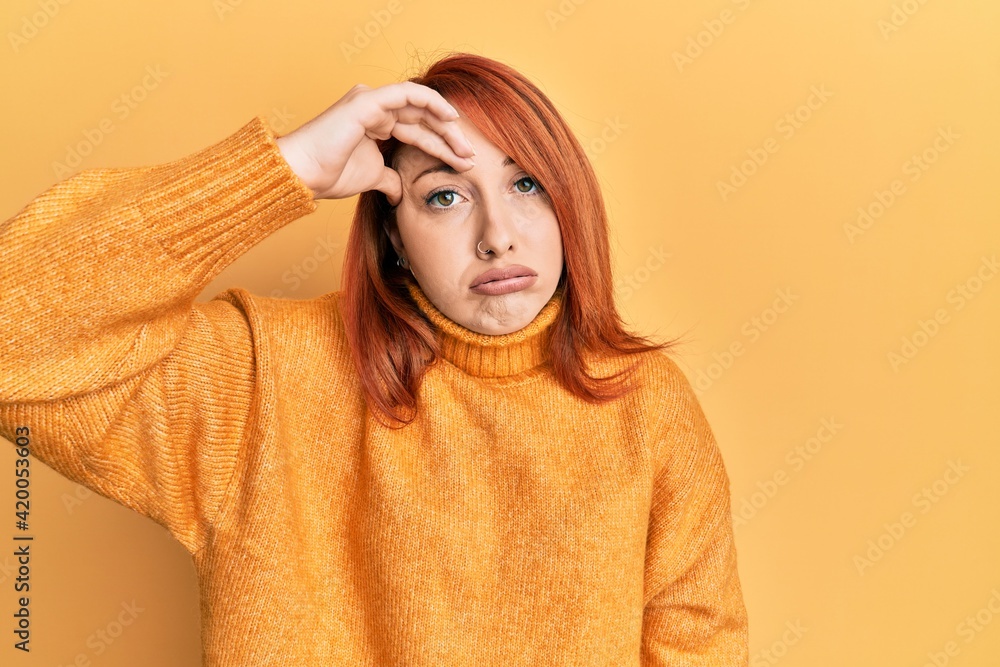 Beautiful redhead woman wearing casual winter sweater over yellow background worried and stressed about a problem with hand on forehead, nervous and anxious for crisis Beautiful redhead woman wearing casual winter sweater over yellow background worried and stressed about a problem with hand on forehead, nervous and anxious for crisis