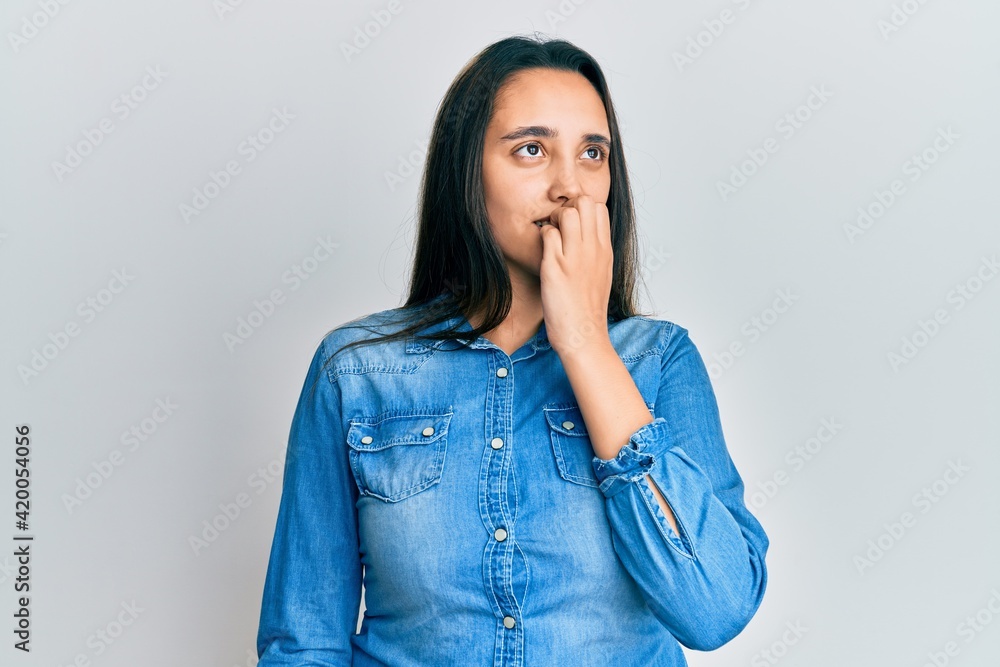 Young hispanic woman wearing casual denim jacket looking stressed and nervous with hands on mouth biting nails. anxiety problem. Young hispanic woman wearing casual denim jacket looking stressed and nervous with hands on mouth biting nails. anxiety problem.