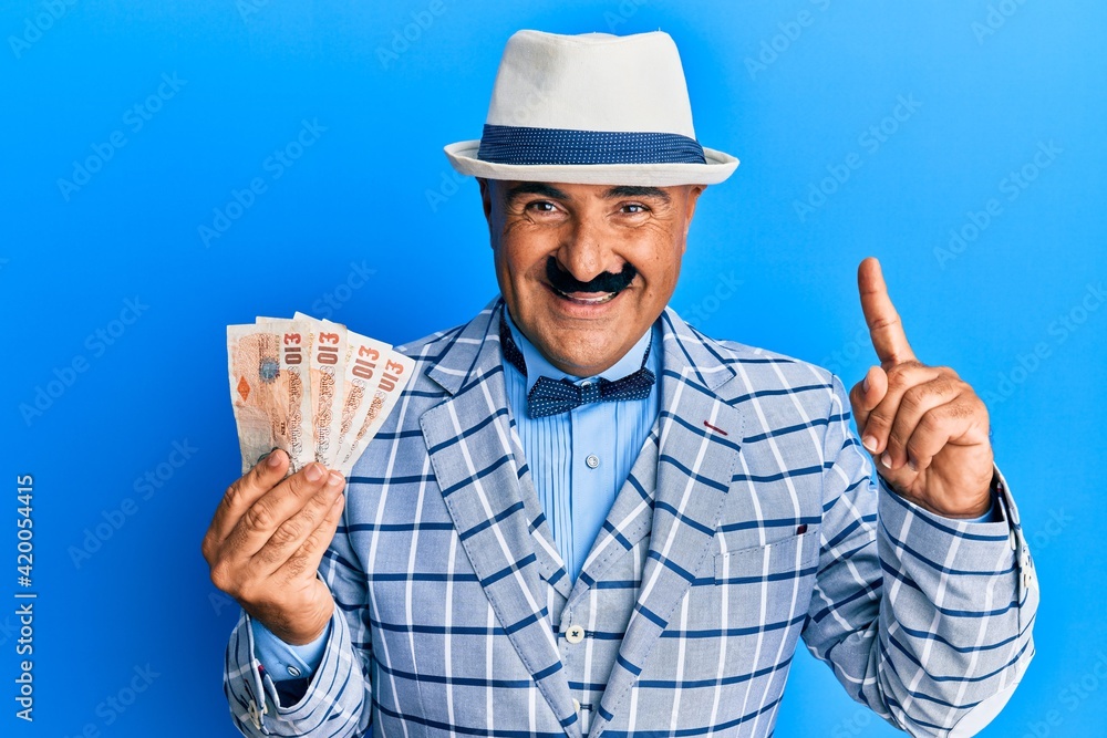 Mature middle east man with mustache wearing elegant vintage style holding pounds banknotes smiling with an idea or question pointing finger with happy face, number one Mature middle east man with mustache wearing elegant vintage style holding pounds banknotes smiling with an idea or question pointing finger with happy face, number one