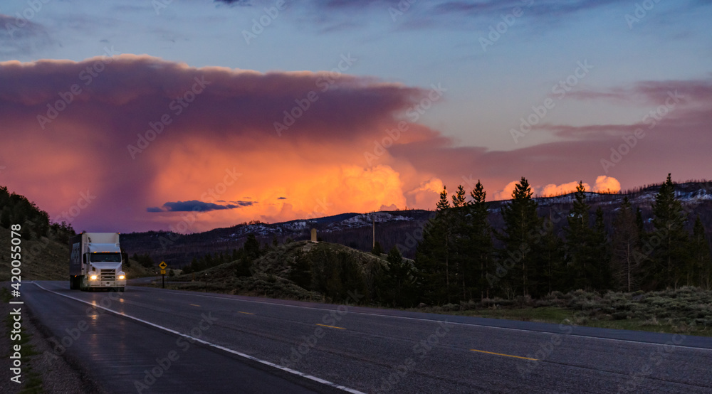 Fototapeta premium Beautiful red sunset over the mountains, car on the road. US
