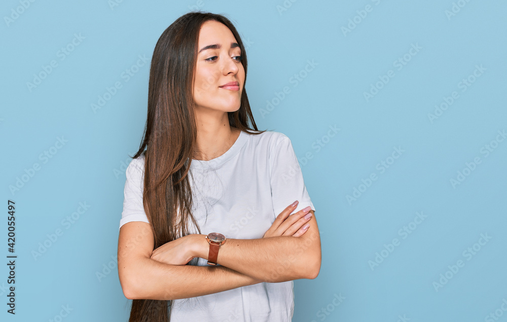 Obraz premium Young hispanic girl wearing casual white t shirt looking to the side with arms crossed convinced and confident