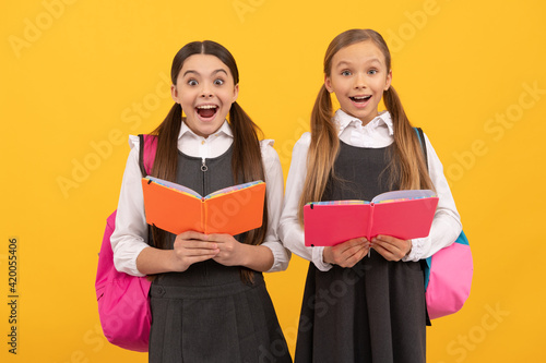 Surprised children in formal uniforms read school books yellow background, library photo