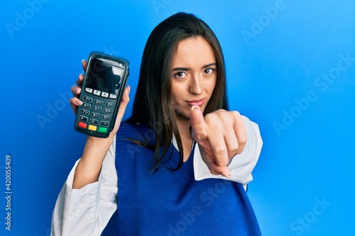 Young hispanic girl holding dataphone pointing with finger to the camera and to you, confident gesture looking serious photo