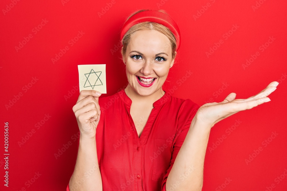 Young blonde woman holding jew star reminder celebrating victory with happy smile and winner expression with raised hands Young blonde woman holding jew star reminder celebrating victory with happy smile and winner expression with raised hands