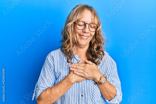 Middle age blonde woman wearing casual clothes and glasses smiling with hands on chest with closed eyes and grateful gesture on face. health concept.