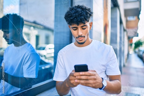 Young arab man with serious expression using smartphone leaning on the wall.
