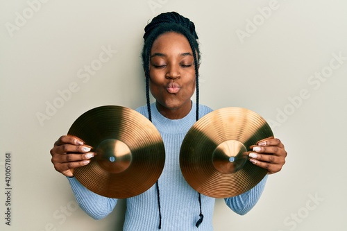African american woman with braided hair holding golden cymbal plates looking at the camera blowing a kiss being lovely and sexy. love expression.