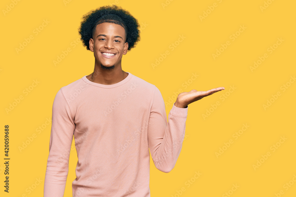 African american man with afro hair wearing casual clothes smiling cheerful presenting and pointing with palm of hand looking at the camera. African american man with afro hair wearing casual clothes smiling cheerful presenting and pointing with palm of hand looking at the camera.