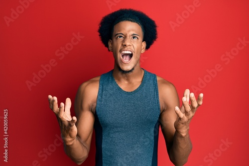 African american man with afro hair wearing sportswear crazy and mad shouting and yelling with aggressive expression and arms raised. frustration concept.