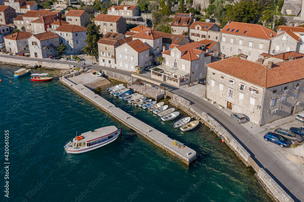 Aerial shot of the old coastal town of Perast. Seaside promenade, residential buildings with traditional balkan red roofs, small marina with boats. Perast, Montenegro