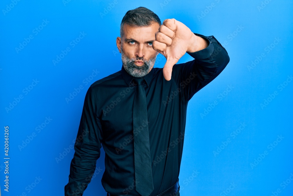 Middle age handsome man wearing business shirt and tie looking unhappy and angry showing rejection and negative with thumbs down gesture. bad expression. Middle age handsome man wearing business shirt and tie looking unhappy and angry showing rejection and negative with thumbs down gesture. bad expression.