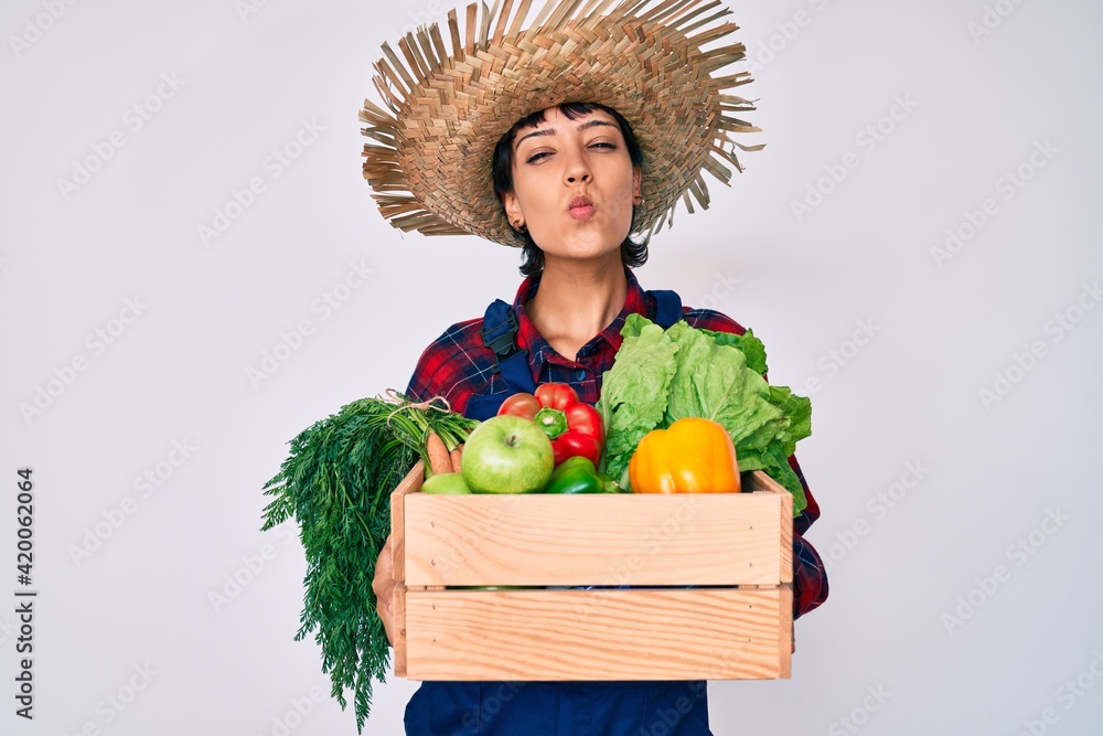Beautiful brunettte woman wearing farmer clothes holding vegetables looking at the camera blowing a kiss being lovely and sexy. love expression.