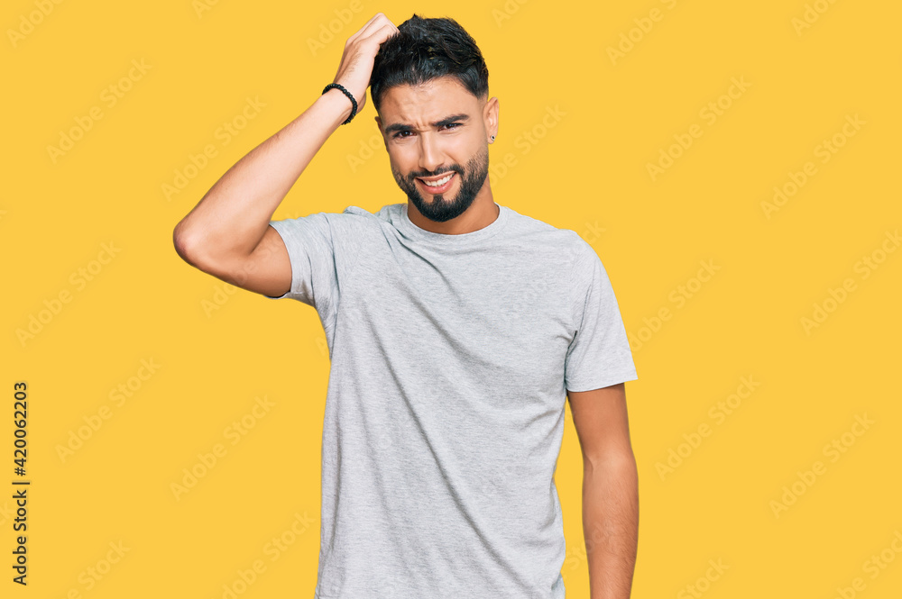 Young man with beard wearing casual grey tshirt confuse and wonder about question. uncertain with doubt, thinking with hand on head. pensive concept. Young man with beard wearing casual grey tshirt confuse and wonder about question. uncertain with doubt, thinking with hand on head. pensive concept.