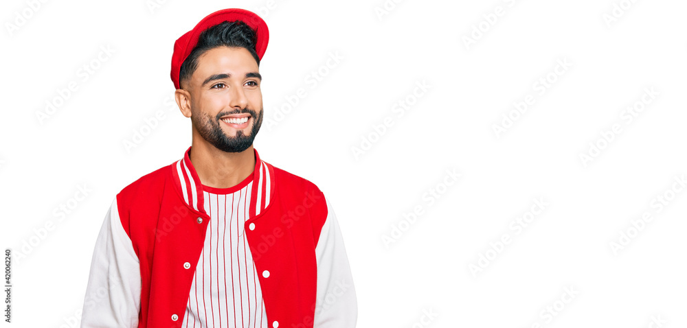 Young man with beard wearing baseball uniform looking away to side with smile on face, natural expression. laughing confident. Young man with beard wearing baseball uniform looking away to side with smile on face, natural expression. laughing confident.