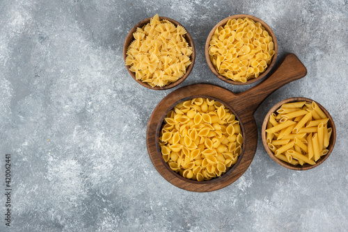 Wooden bowl of raw various pasta on marble background