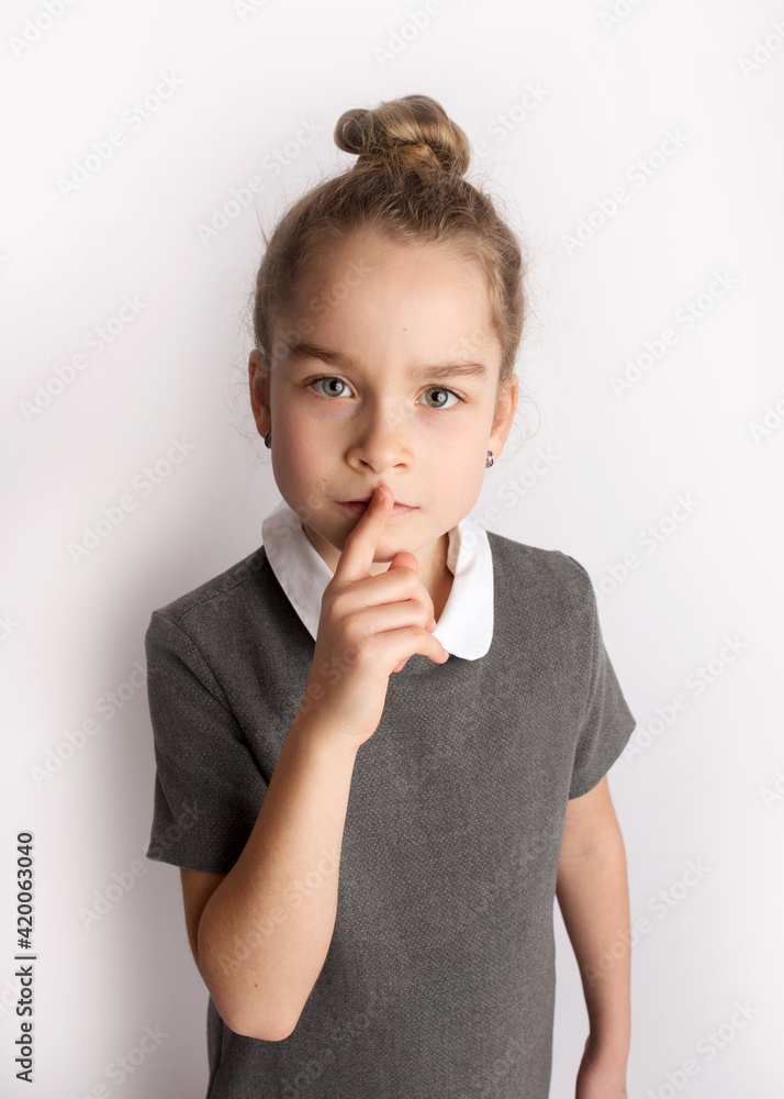 Attractive little girl in a strict school dress, stands on a white background with empty copy space, gestures with her hands, admires a happy expression on her face Attractive little girl in a strict school dress, stands on a white background with empty copy space, gestures with her hands, admires a happy expression on her face