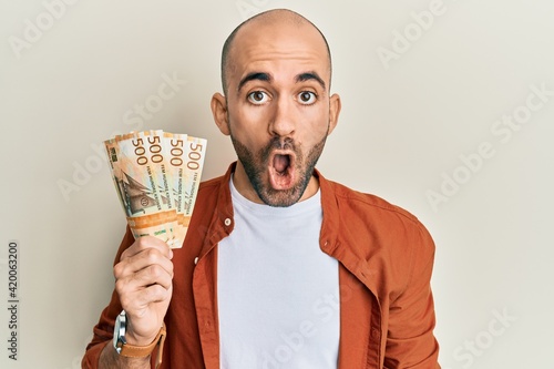 Принти на полотні Young hispanic man holding 500 norwegian krone banknotes scared and amazed with