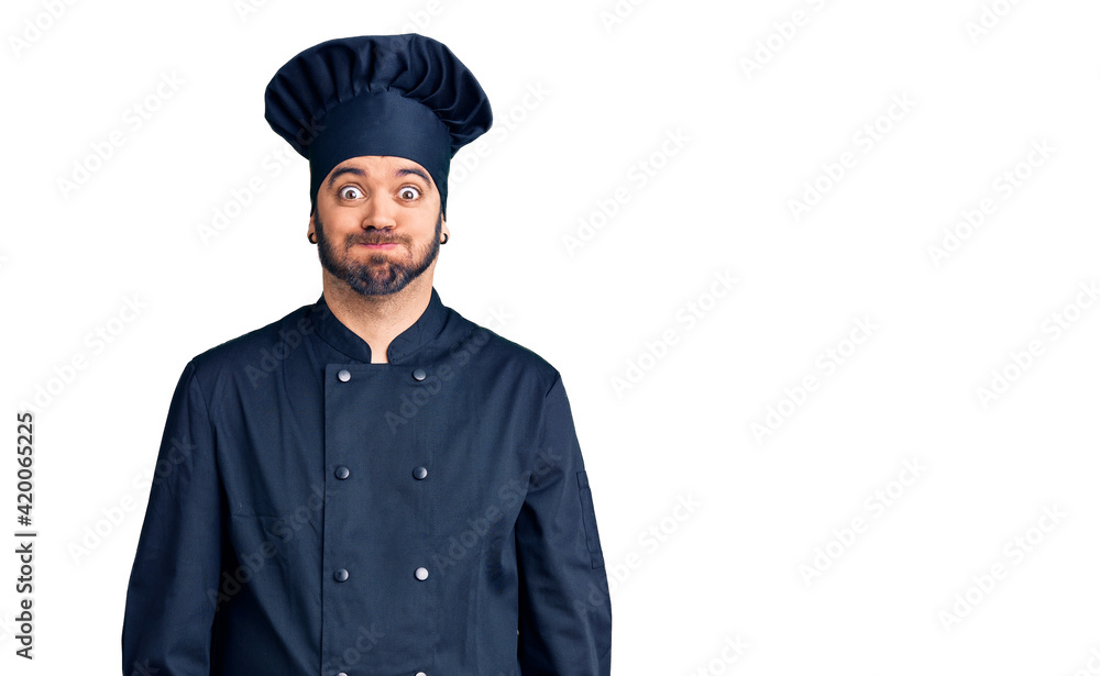 Young hispanic man wearing cooker uniform puffing cheeks with funny face. mouth inflated with air, crazy expression. Young hispanic man wearing cooker uniform puffing cheeks with funny face. mouth inflated with air, crazy expression.
